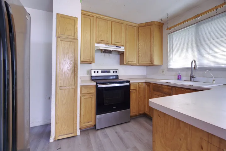Kitchen featuring wood-finish cabinetry, light-toned countertops, stainless steel refrigerator, and wood-finish flooring