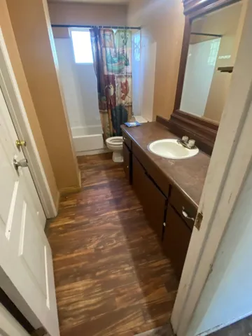 Wood-looking flooring with a vanity featuring built-in cabinetry, a drop-in sink, and a framed mirror