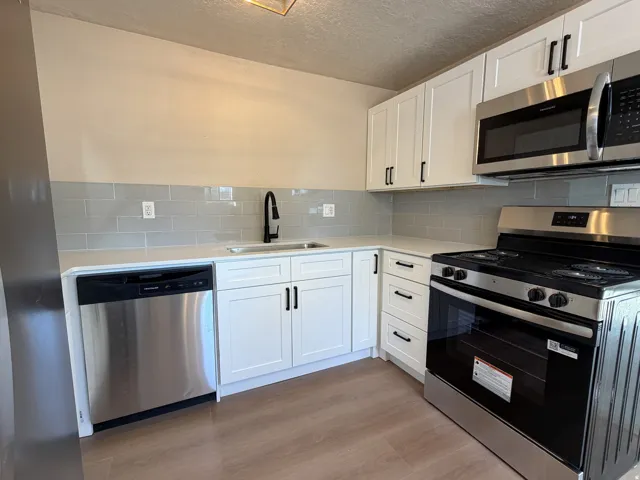 Kitchen featuring white shaker cabinetry, stainless steel appliances, light-toned countertops, a subway tile backsplash, and wood-finish flooring