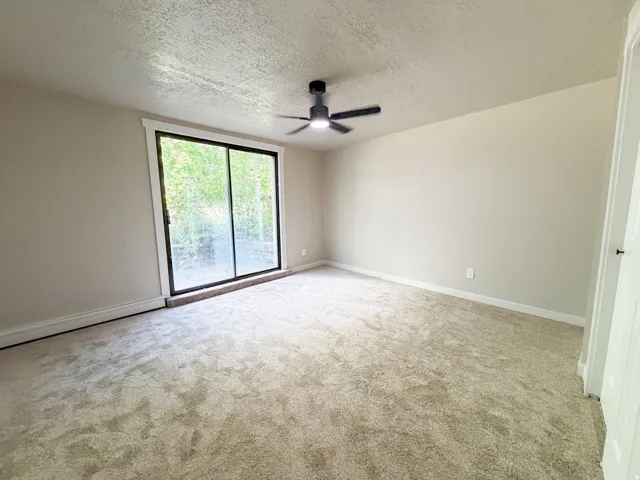 Bedroom 1. Spacious room featuring neutral carpeting, light-toned walls, and a ceiling fan