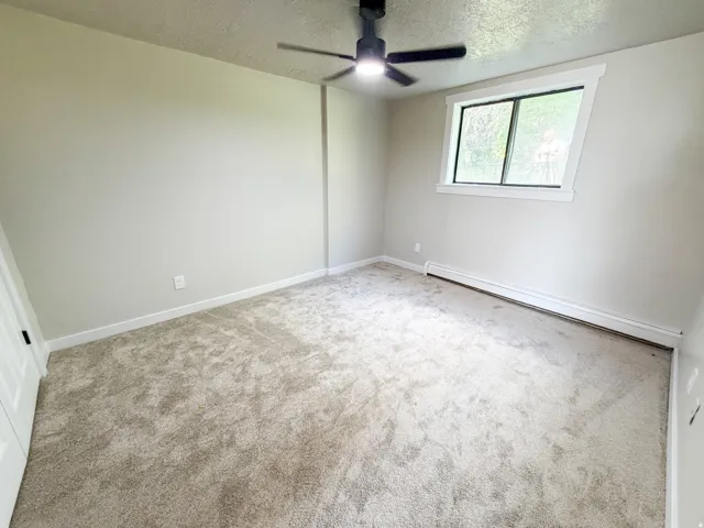 Bedroom 2. Spacious bedroom featuring neutral carpeting, abundant natural light from a large window, ceiling fan with integrated lighting, and fresh white walls throughout