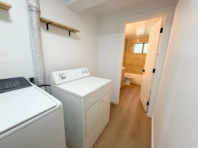 Laundry area featuring wood-finish flooring and two wall-mounted shelves