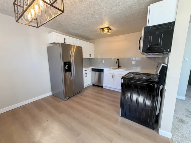 Kitchen featuring wood-finish flooring, white cabinetry with black hardware, stainless steel refrigerator and dishwasher, and a black electric range with an overhead microwave