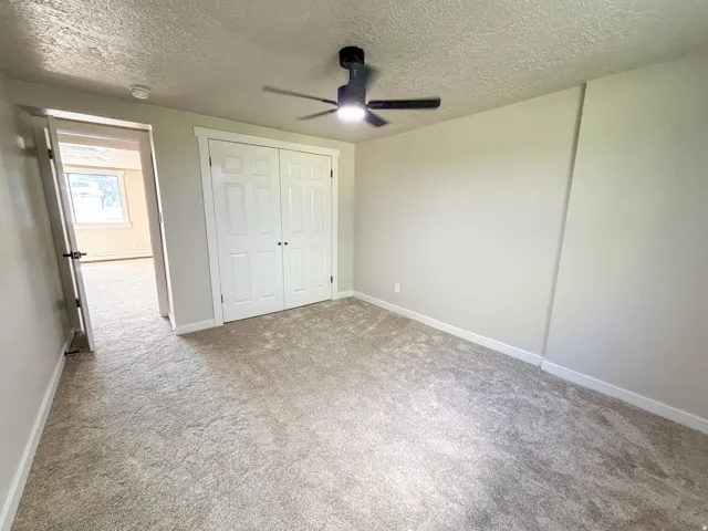 Bedroom 2. Light-toned carpet flooring, white painted walls, and a ceiling fan with integrated lighting