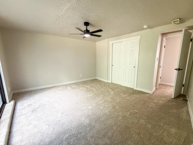 Bedroom 1. Carpeted room featuring a ceiling fan with integrated lighting, a sliding closet door, and a paneled interior door with dark hardware