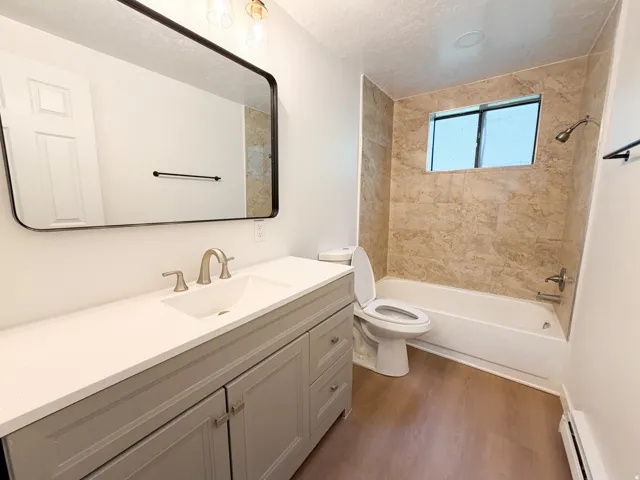 Bathroom featuring a light gray vanity with a single basin sink, brushed nickel faucet, large rectangular mirror, and a bathtub with tiled surround