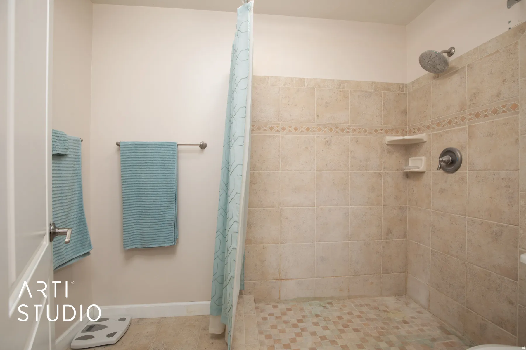 Walk-in shower with neutral tile surround, decorative tile accent band, and built-in corner shelves