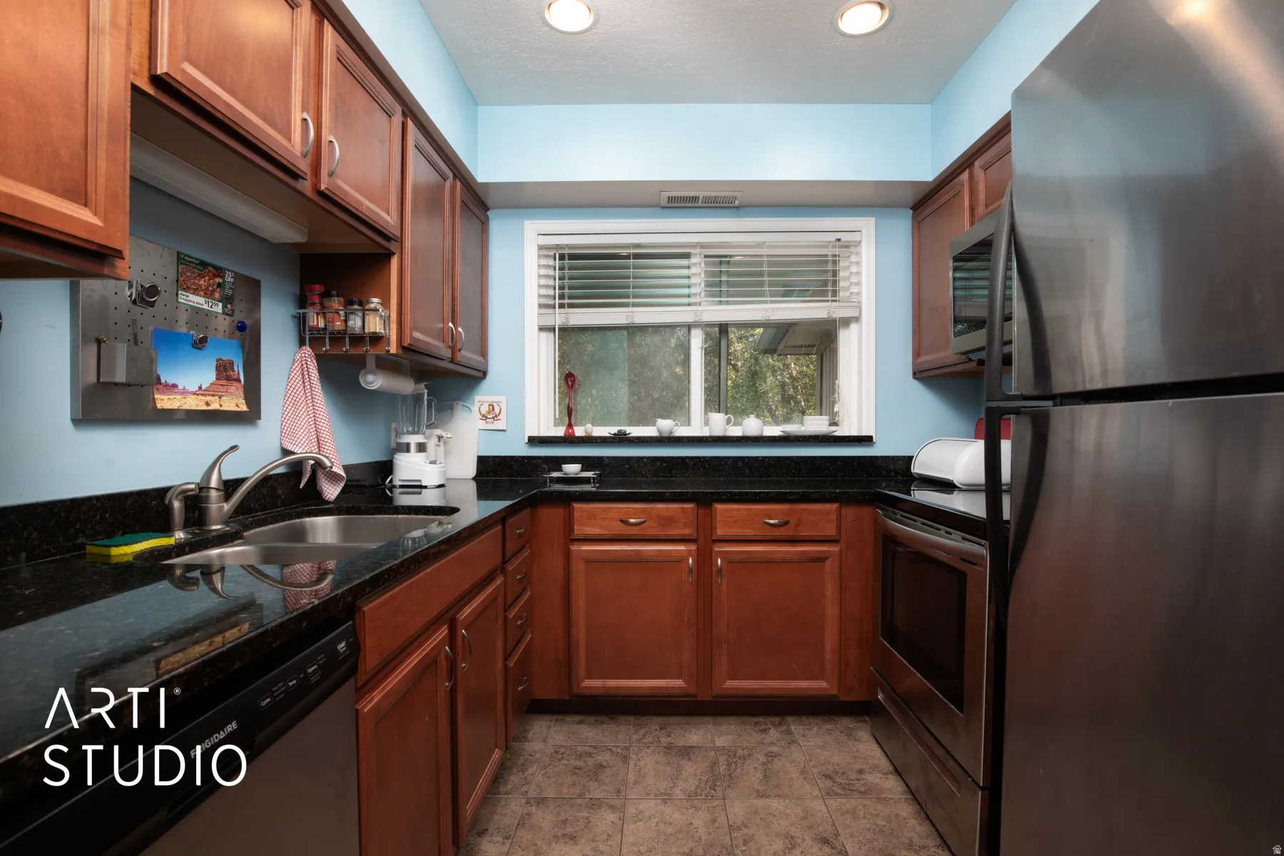 Kitchen featuring wood cabinetry, dark countertops, stainless steel appliances, and a window with blinds