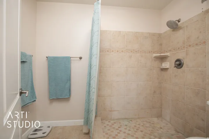 Walk-in shower with neutral tile surround, decorative tile accent band, and built-in corner shelves