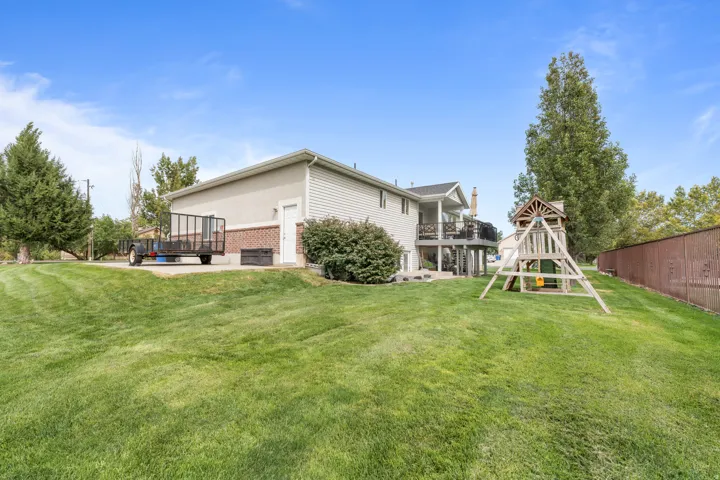 Expansive lawn with mature trees, brick accent siding, and upper-level deck