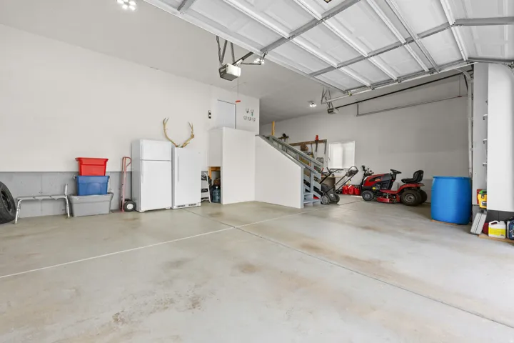 Spacious garage with concrete flooring, overhead lighting, and interior access stairs