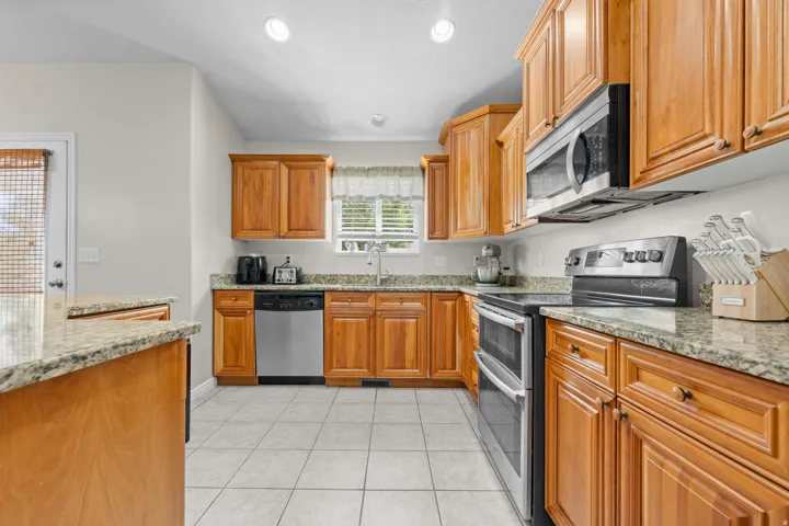 Kitchen featuring wood cabinetry, granite countertops, tile flooring, and stainless steel appliances