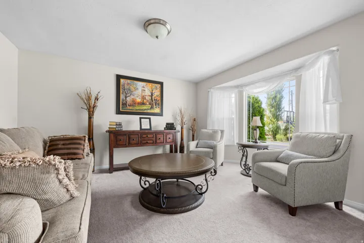 Carpeted living area off entry featuring a bay window, light-toned walls, and a decorative console table