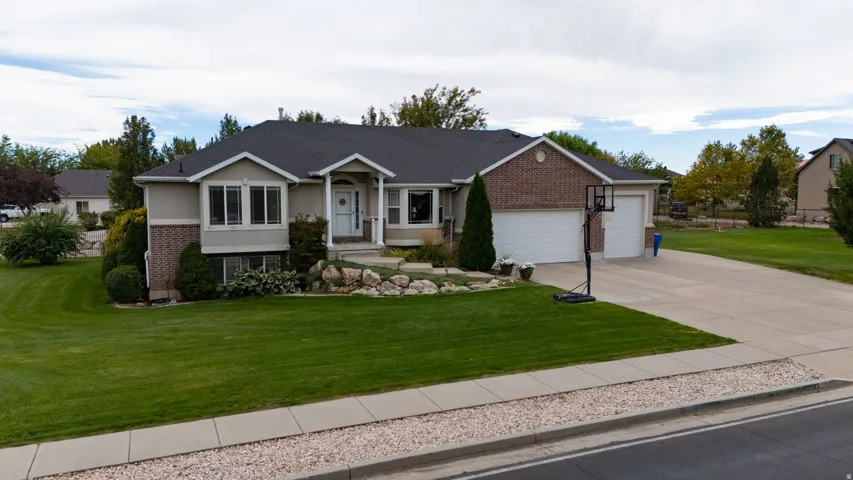 Brick and stucco exterior with a covered entry, attached two-car garage, expansive driveway, and a well-maintained front lawn with established landscaping