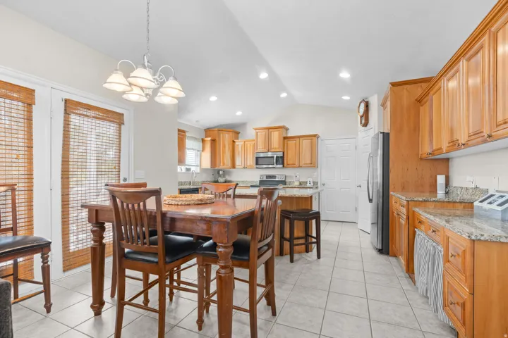 Spacious kitchen and dining area featuring warm wood cabinetry, granite countertops, stainless steel appliances, recessed lighting, and a tile floor