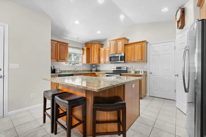 Kitchen featuring wood cabinetry, stainless steel appliances, a multi-level island with seating, and tile flooring