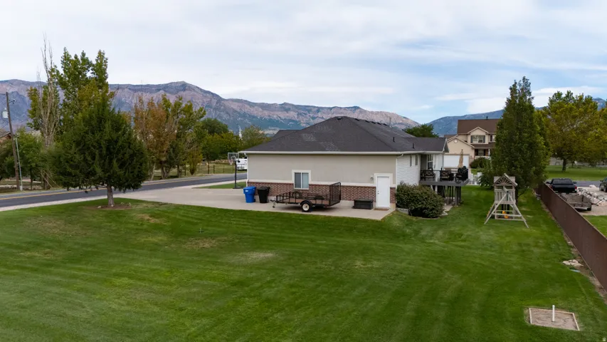 Spacious grassy yard with mature trees, a multi-level deck, and a concrete patio