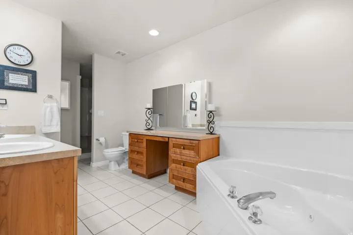 Primary bathroom, white tiled flooring, dual sinks with wood-finish vanities, integrated soaking jetted tub, recessed lighting, and a separate walk in shower