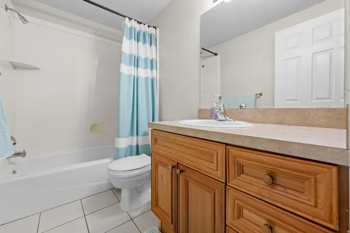 Full basement bathroom with a tub/shower combination, white ceramic tiled flooring, and a wood-finish vanity with a built-in sink