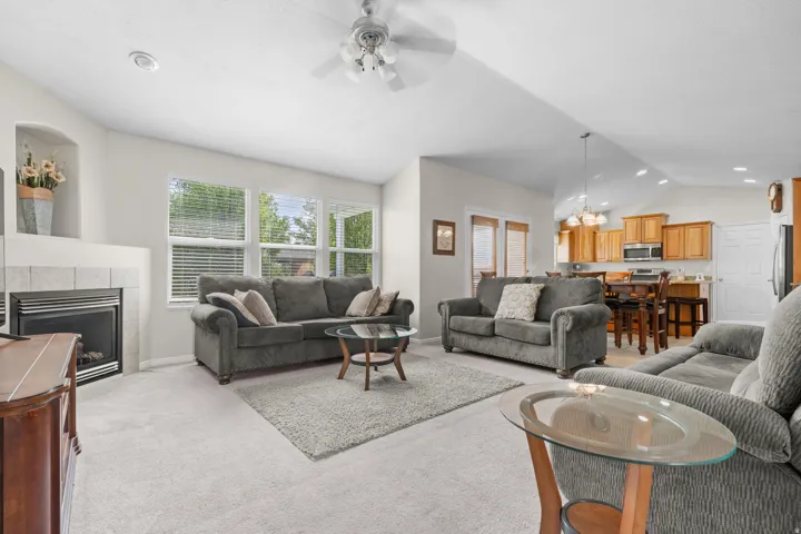 Carpeted living area featuring a tiled gas fireplace with an arched niche, multiple windows, and a ceiling fan