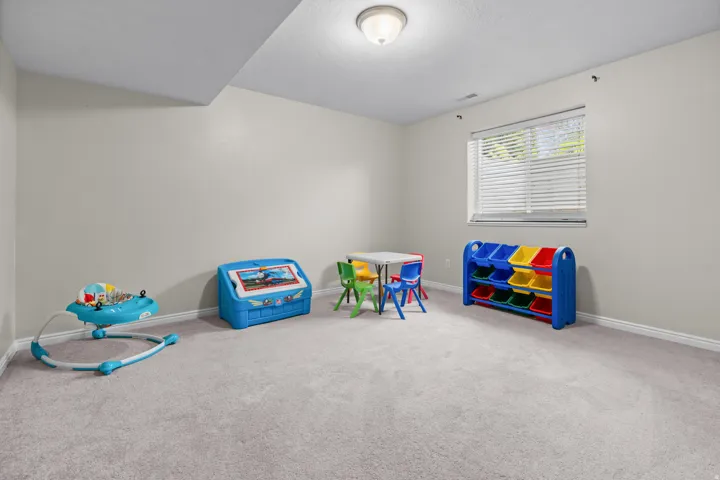 Basement bedroom, carpeted recreation room featuring neutral walls, recessed ceiling lighting, and a large window with plantation shutters allowing natural light throughout the space