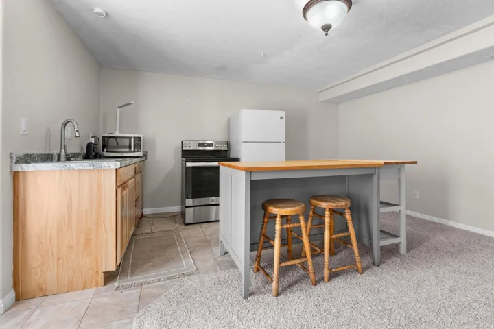 Compact basement kitchen area featuring a stainless steel sink, wood cabinetry, stone-finish countertop, and tile flooring with basement walkout entry