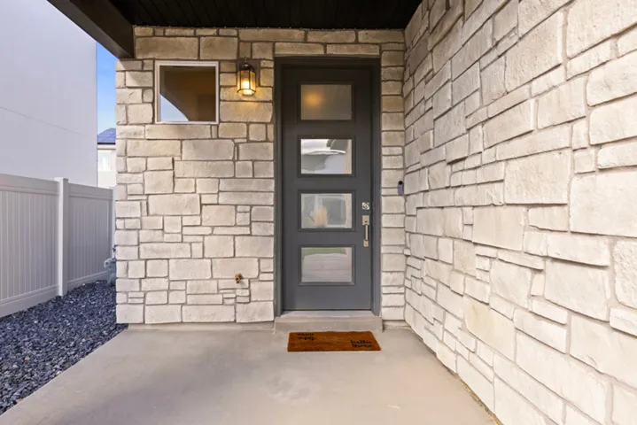 Stone veneer facade, contemporary entry door with frosted glass panels, concrete porch, and dark aggregate landscaping