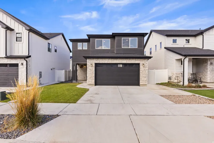 Contemporary exterior featuring a dark facade, stone accents, attached garage, concrete driveway, and a manicured lawn - Call for your showing today!