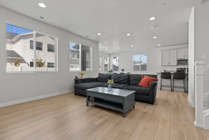 Open-concept living area with wood-finish flooring, recessed lighting, and multiple windows with blinds