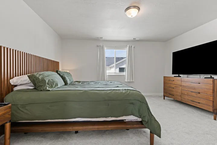 Spacious primary bedroom with a ceiling-mounted light fixture and a window with blinds