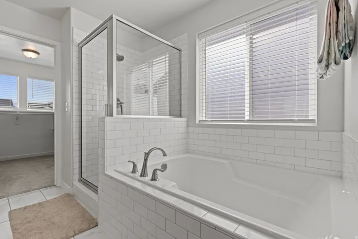 Built-in soaking tub with subway tile surround, glass-enclosed shower, dual windows with blinds, and brushed nickel fixtures