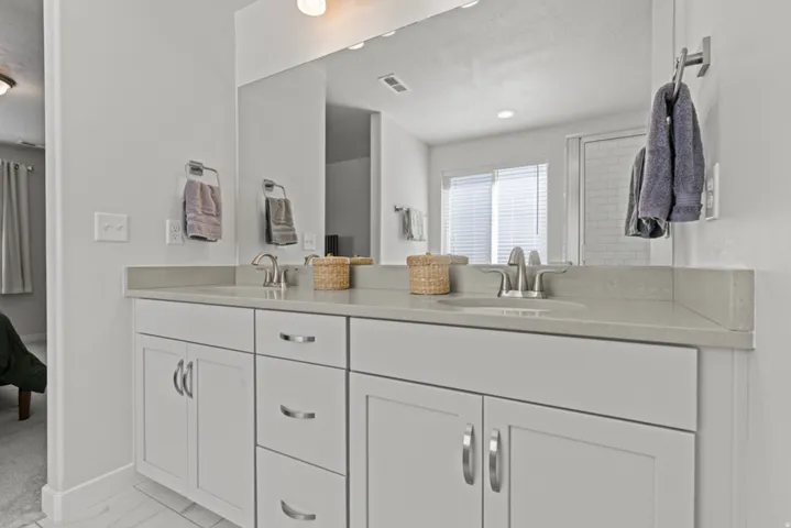 Primary bathroom with dual vanity with white cabinetry, light gray countertop, and undermount sinks