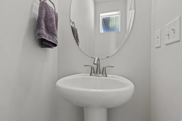 1/2 bathroom with a pedestal sink with a brushed nickel faucet, oval wall mirror, and a small window