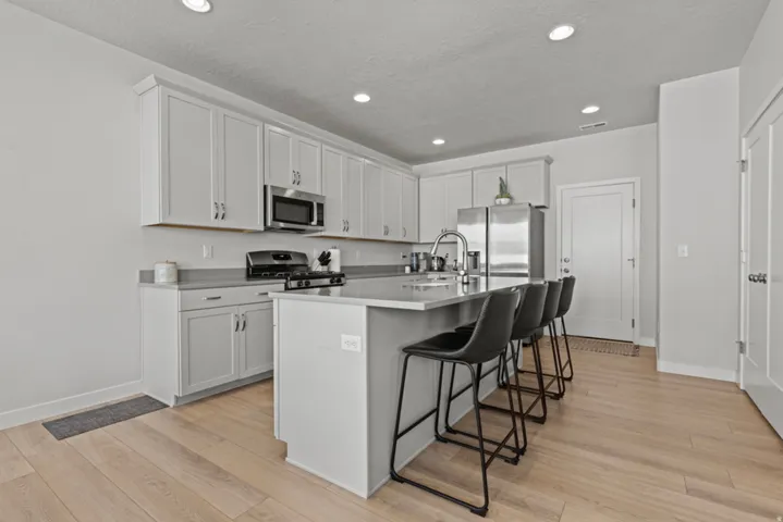 Kitchen featuring light wood-finish flooring, recessed lighting, white cabinetry, a kitchen island with seating, and stainless steel appliances