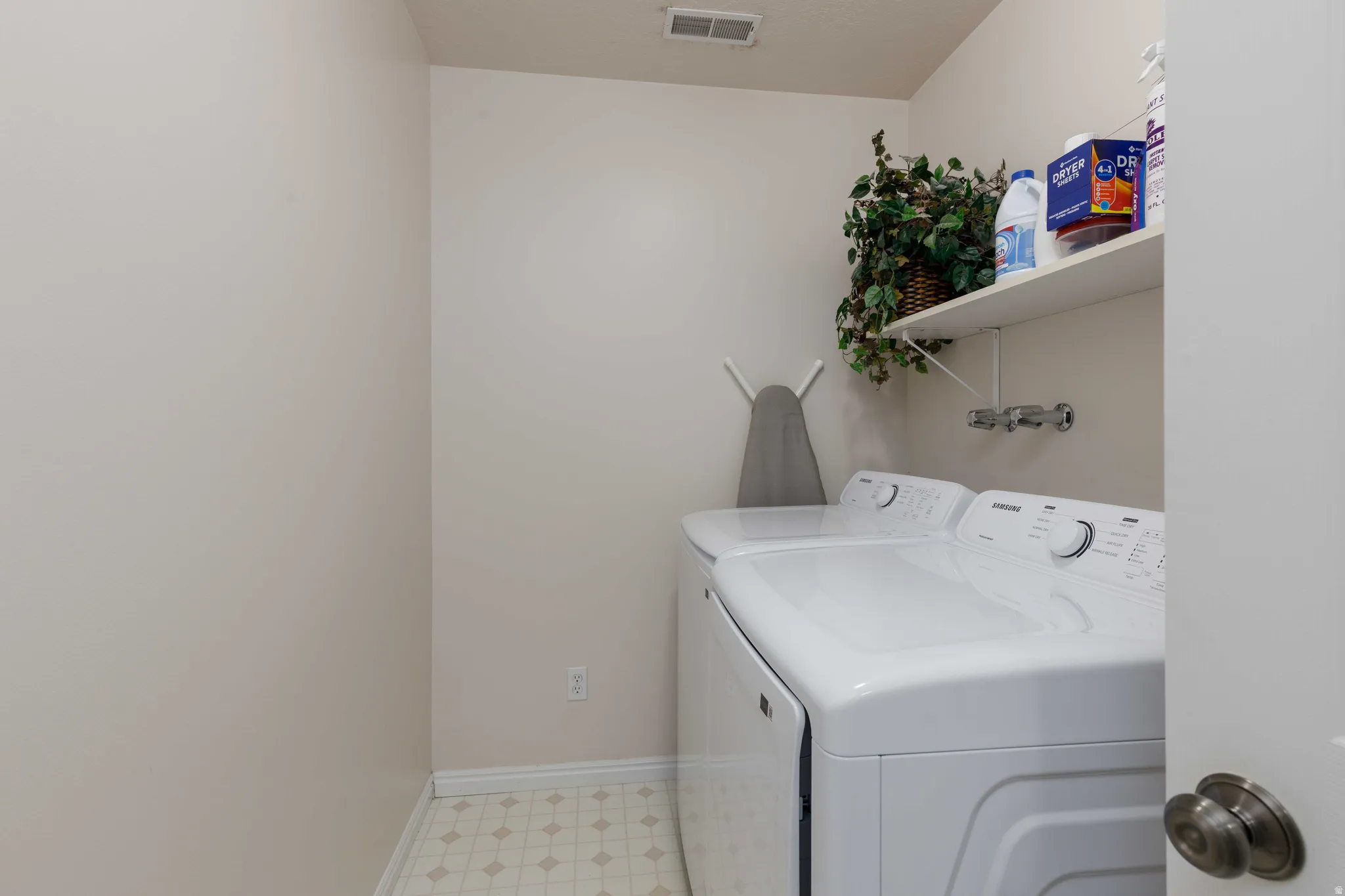 Dedicated laundry room featuring side-by-side washer and dryer hookups, tile flooring, wall-mounted faucet with basin, open shelving with decorative accents, and bright recessed lighting