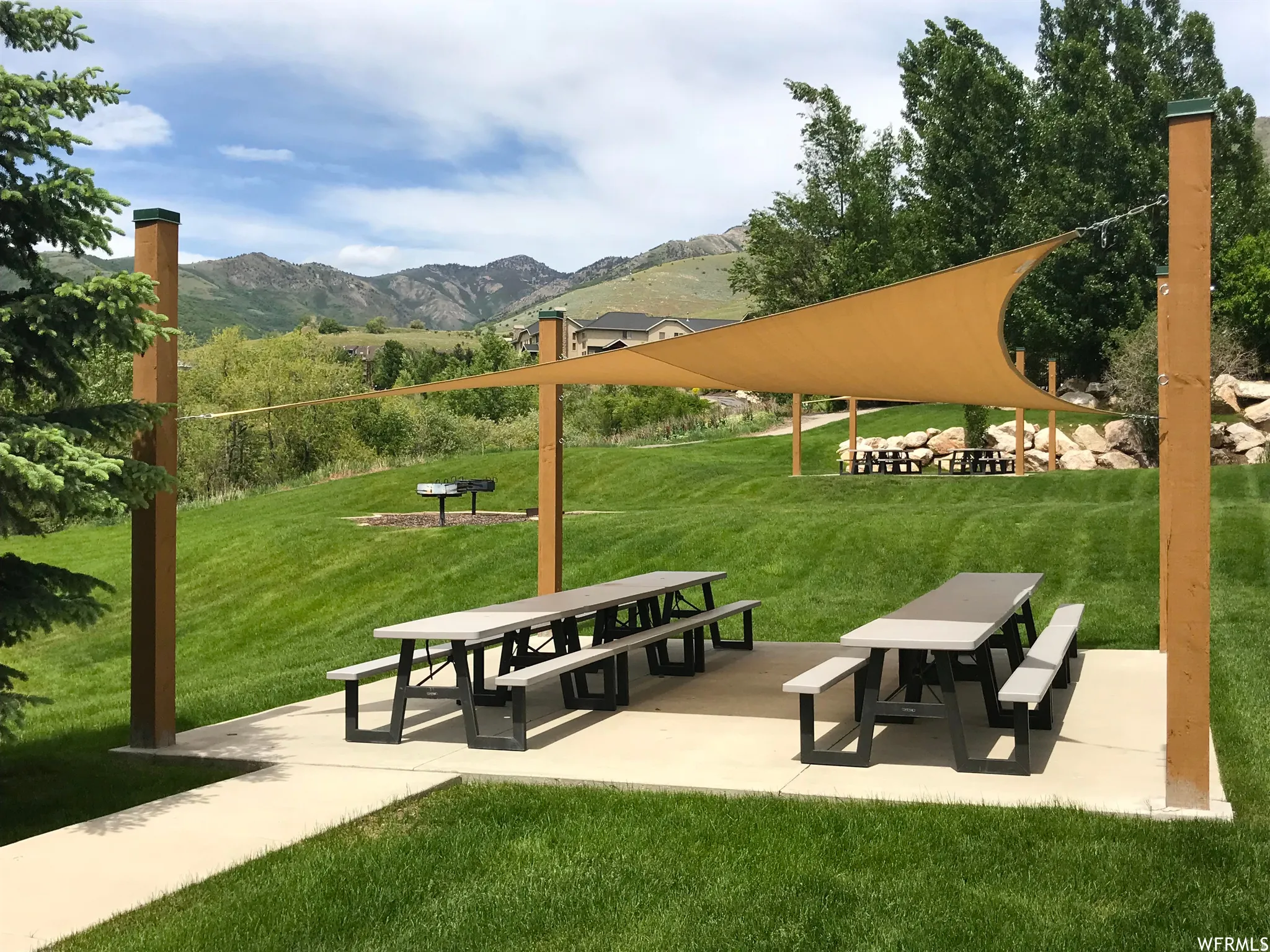 Outdoor common area featuring multiple picnic tables, a shade sail structure, a built-in grill, and expansive grassy spaces