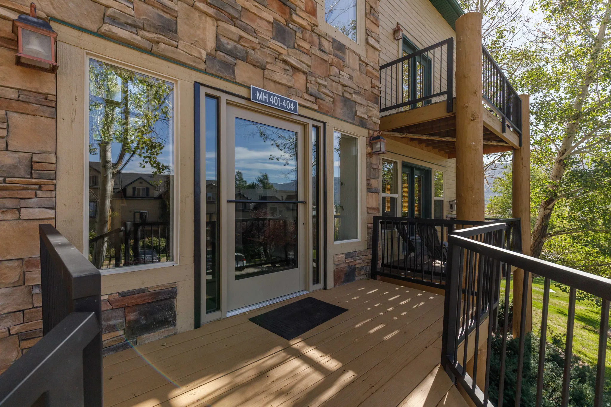 Stacked stone exterior with a private outdoor deck featuring black metal railings and natural wood support columns