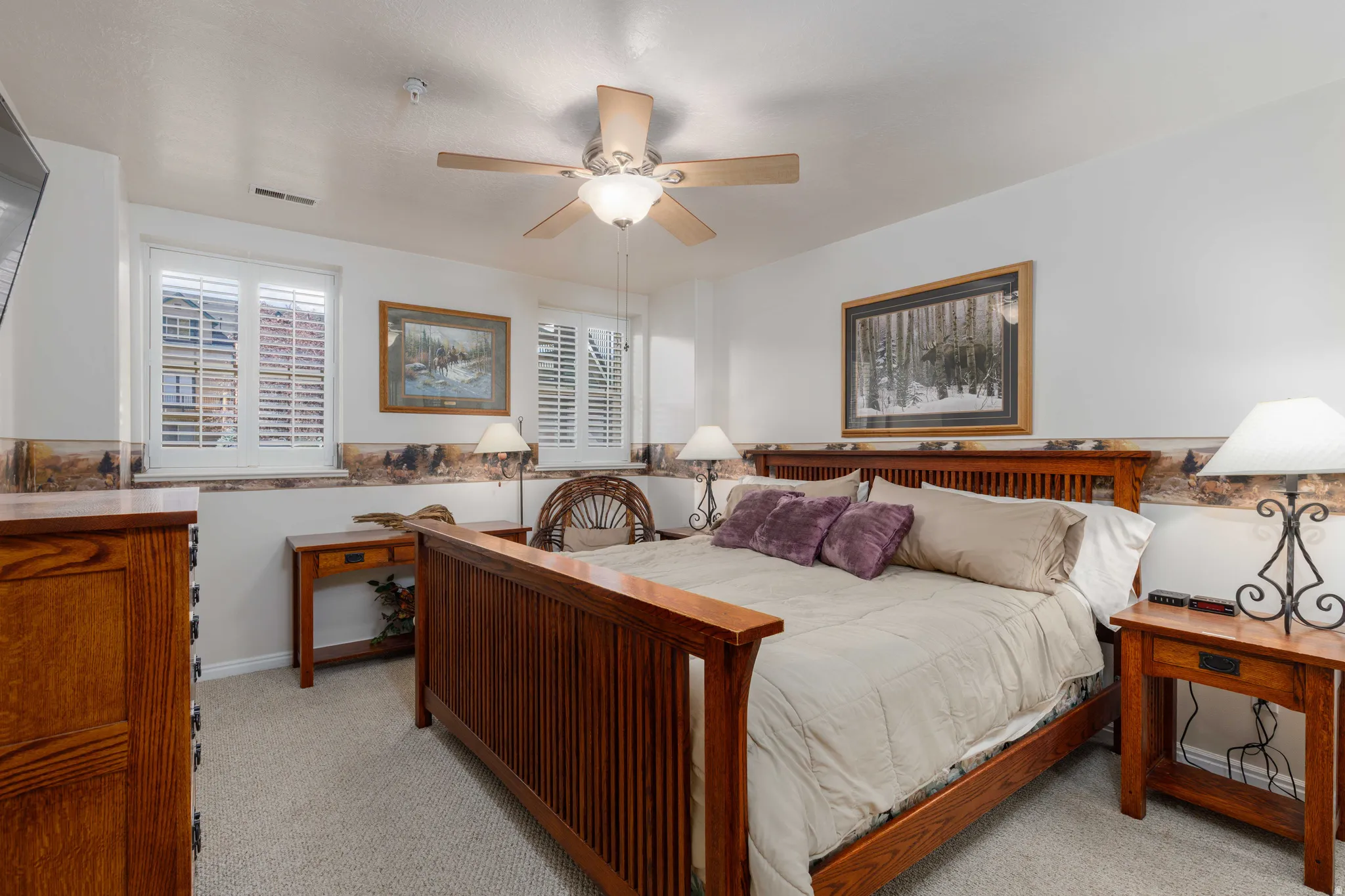 Spacious primary bedroom featuring wood-finish flooring, ceiling fan with integrated lighting, plantation shutters, and wood-frame bed with coordinating nightstands