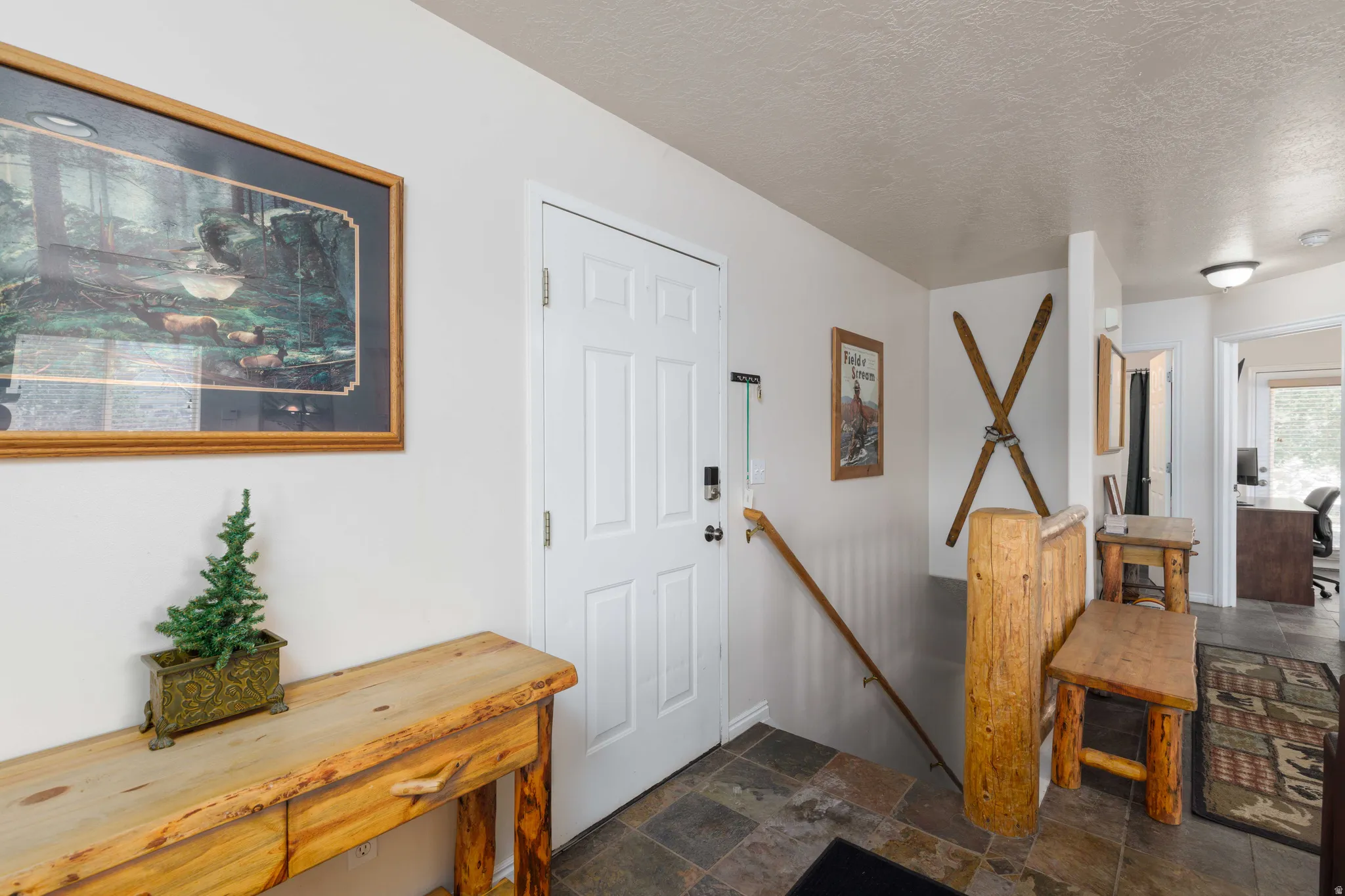 Panel-style entry door, slate tile flooring, wood railing, and recessed ceiling light fixture
