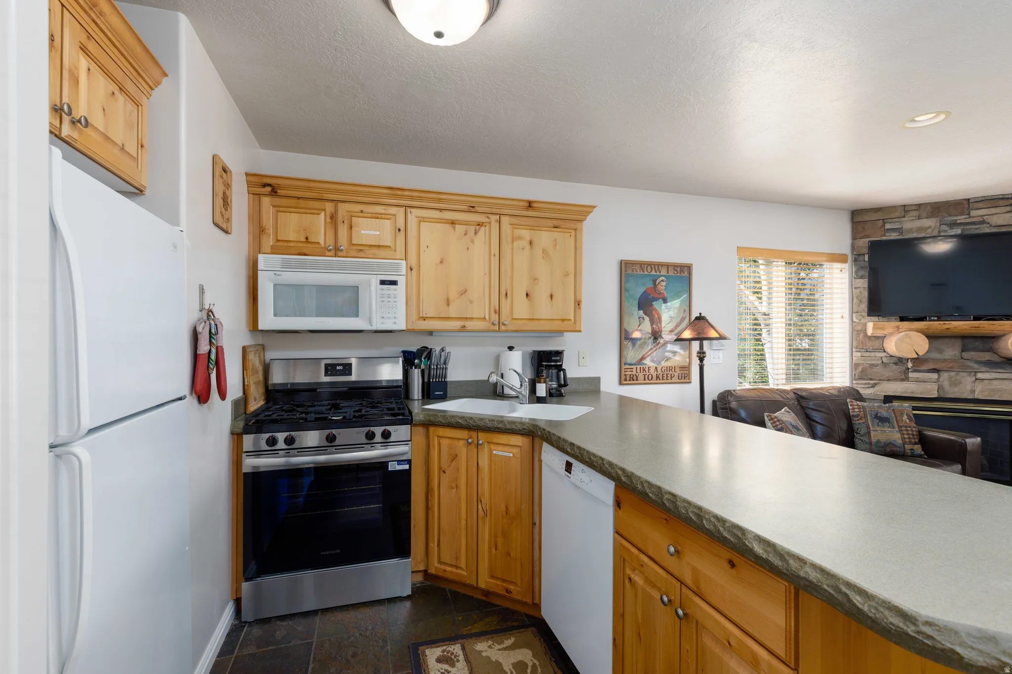Warm wood cabinetry, integrated stainless steel range with overhead microwave, and a durable countertop extending to a breakfast bar