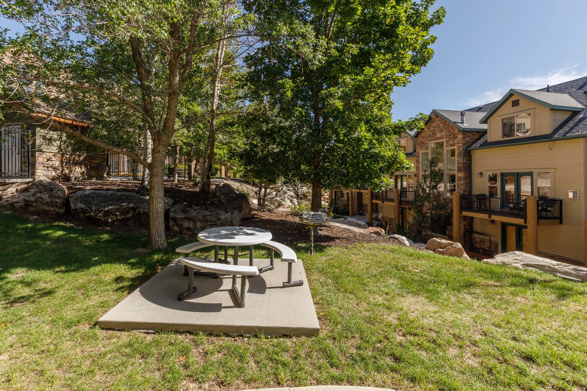 Expansive outdoor space featuring a concrete pad, mature trees, and natural rock landscaping