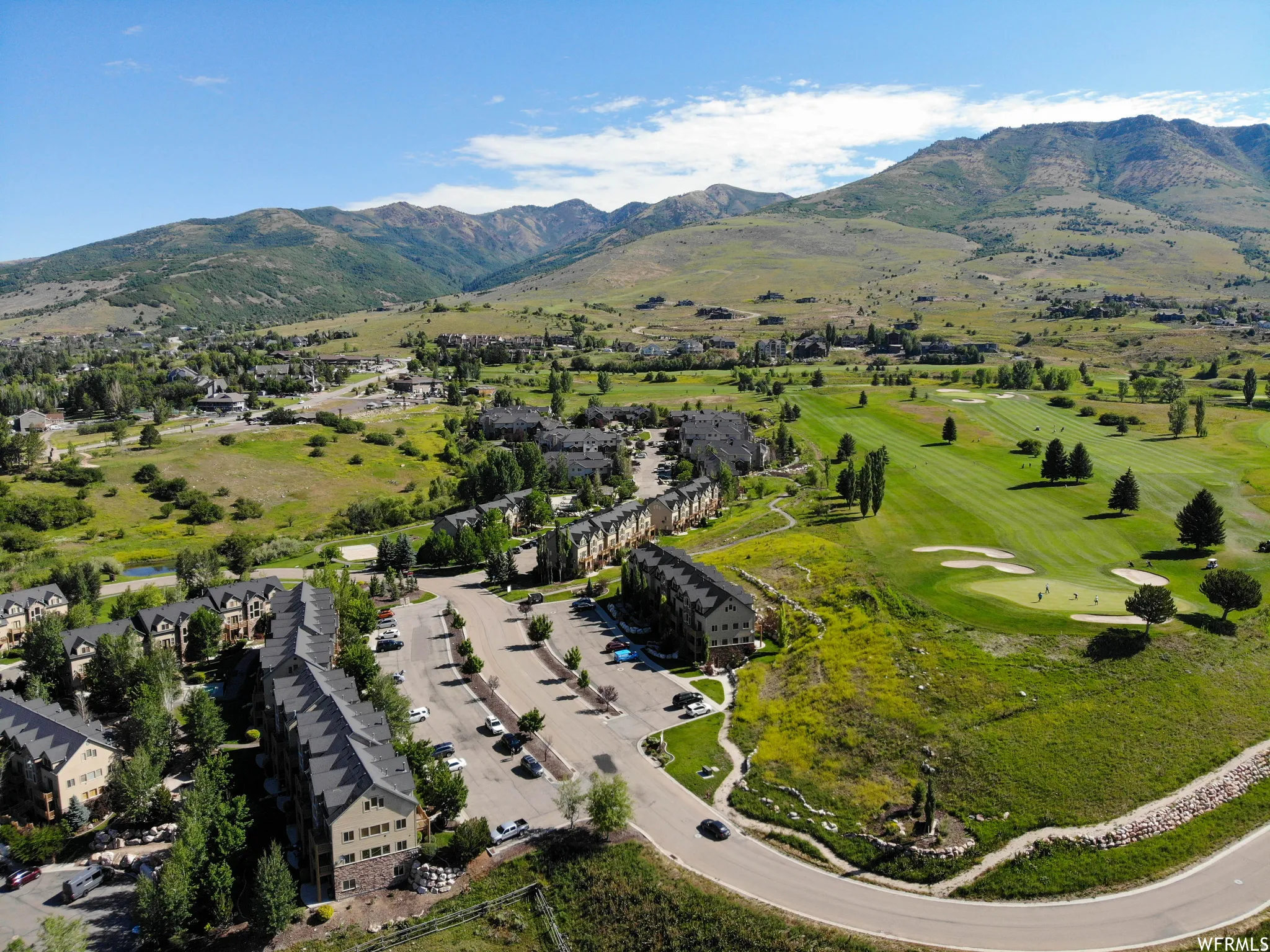 Townhome community with mountain scenery, adjacent to a golf course, featuring mature trees and paved roadways