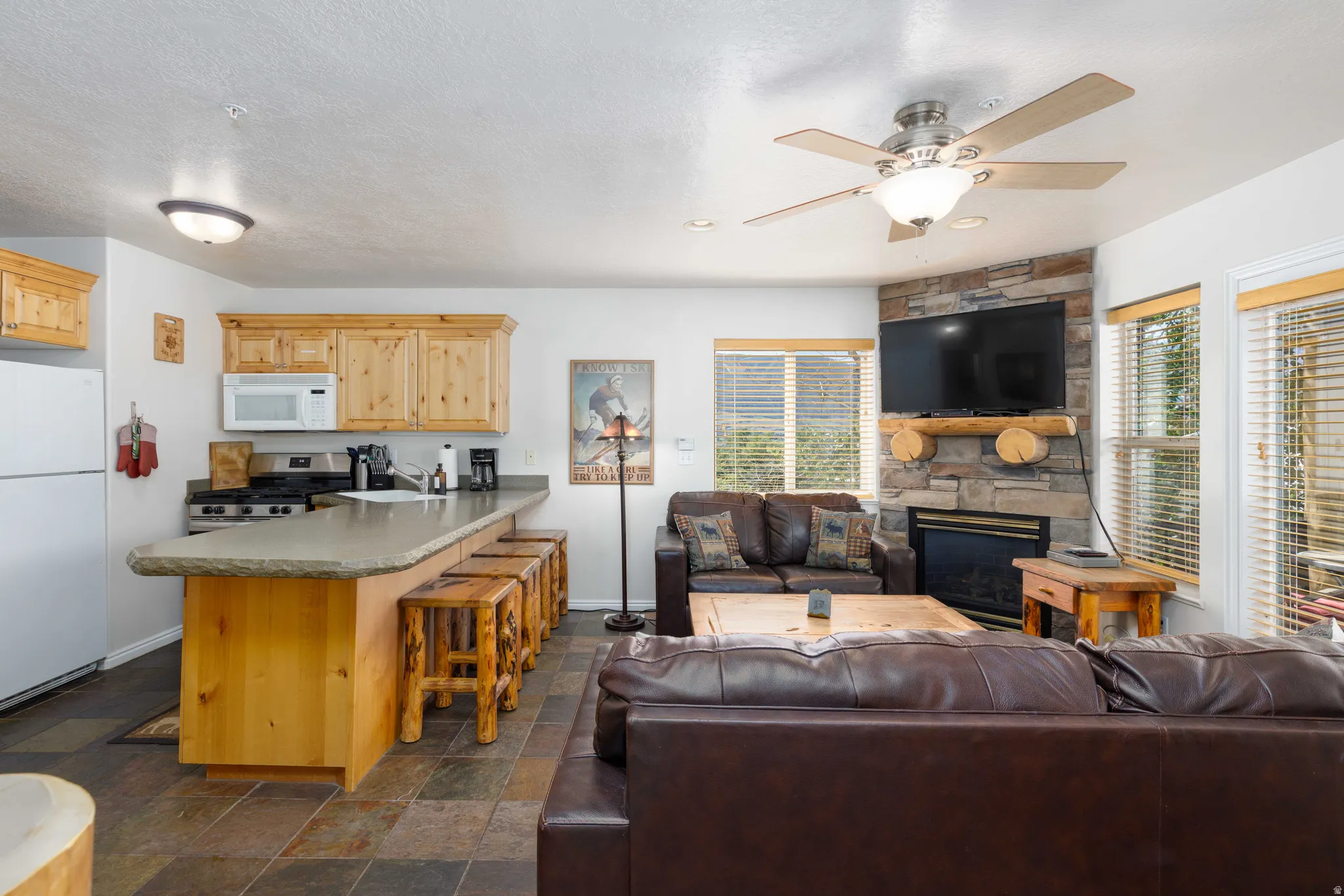 Open-concept living area featuring a stone-faced fireplace, wood-finish mantel, and ceiling fan