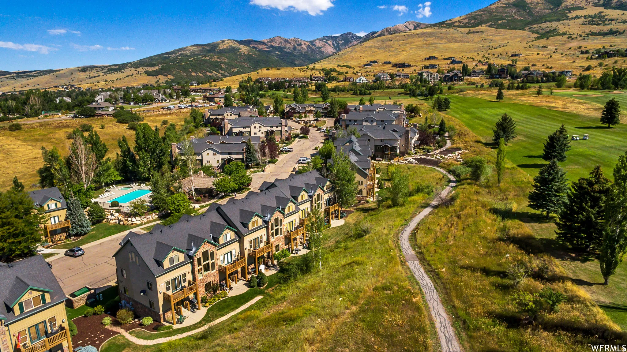 Townhome community featuring a swimming pool, adjacent golf course, and mountain backdrop