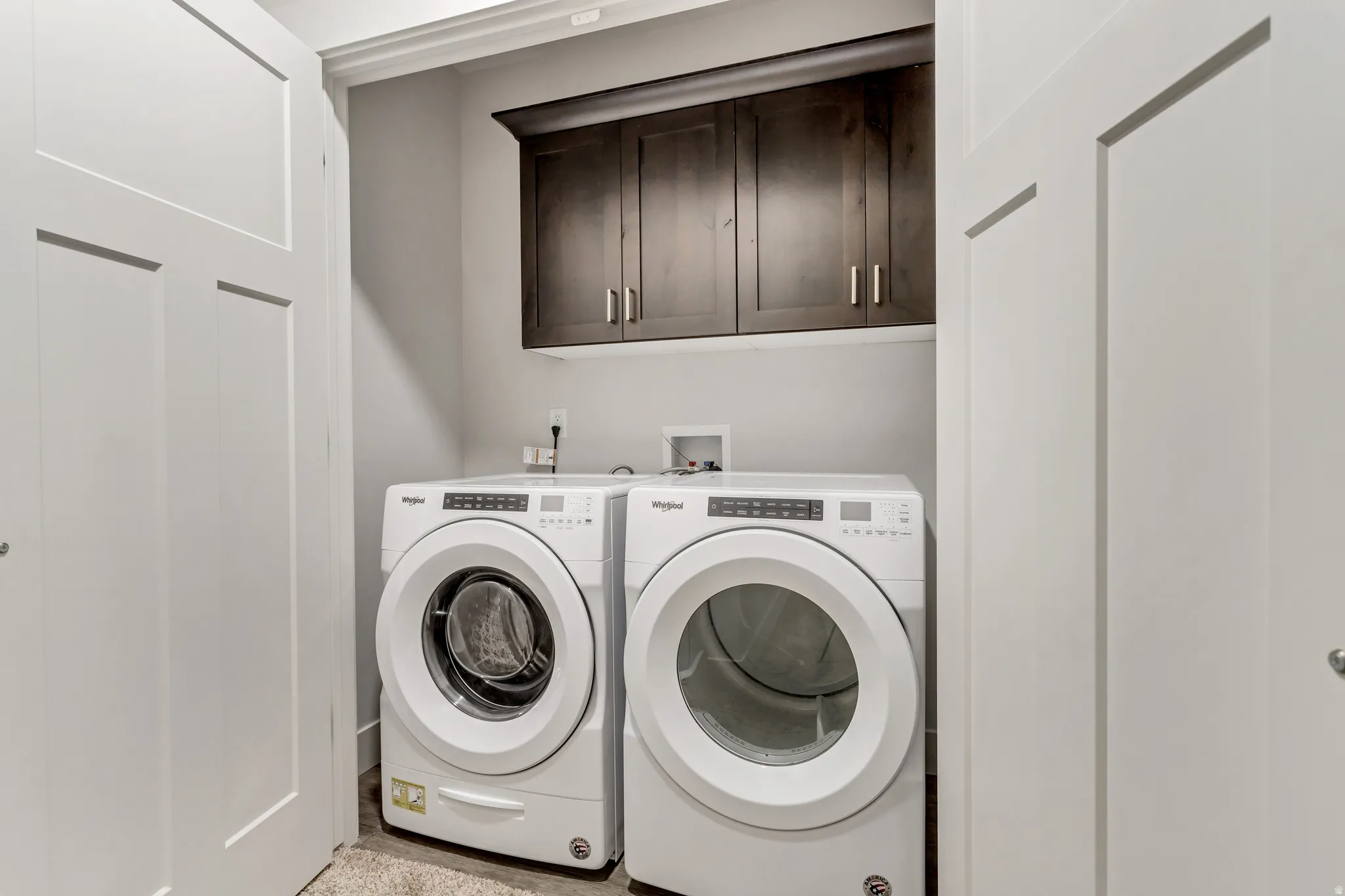 Laundry area featuring built-in dark wood cabinetry, white front-loading washer and dryer, and white paneled bi-fold doors