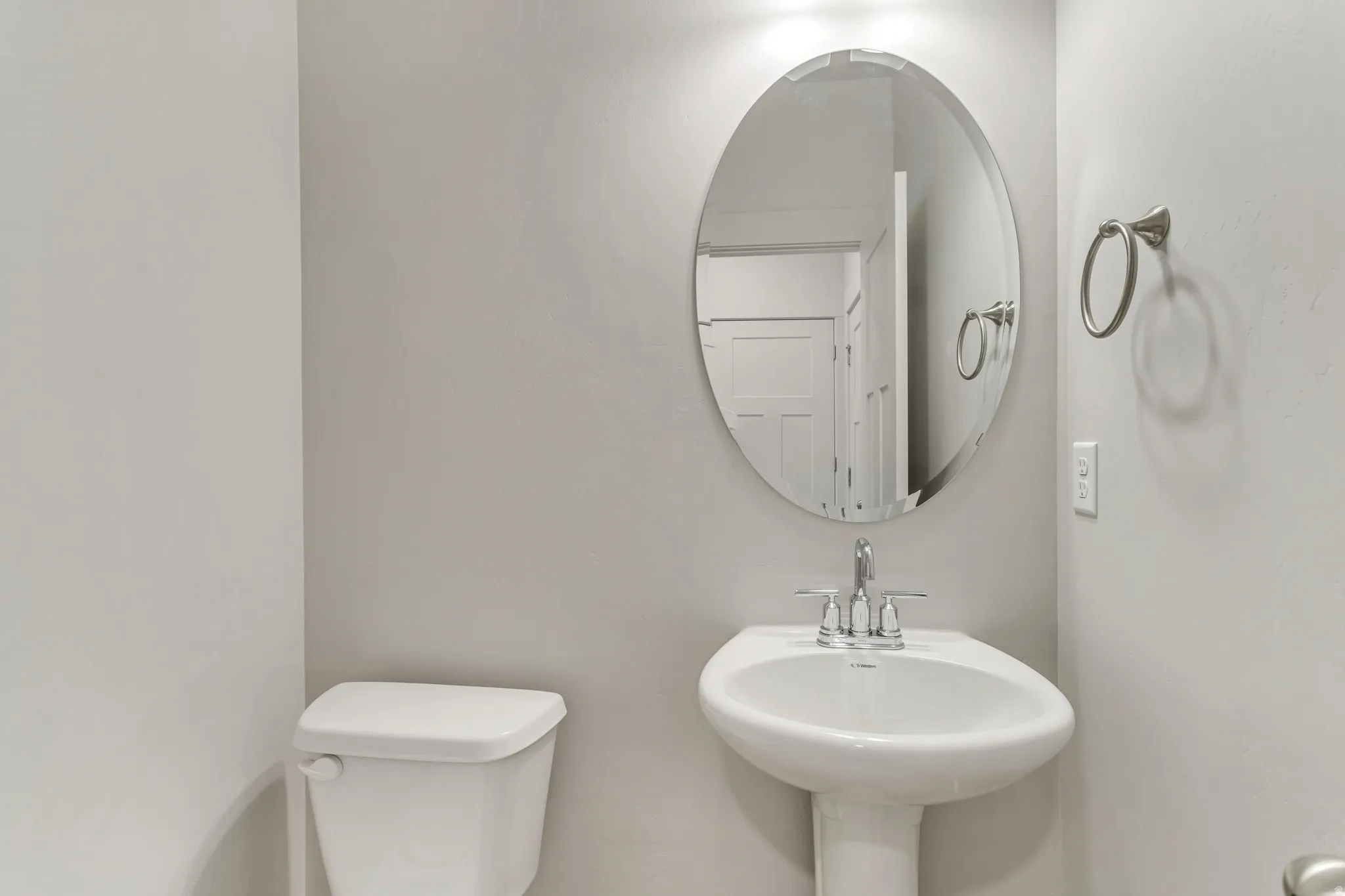 Pedestal sink with chrome faucet, oval mirror, and a white toilet