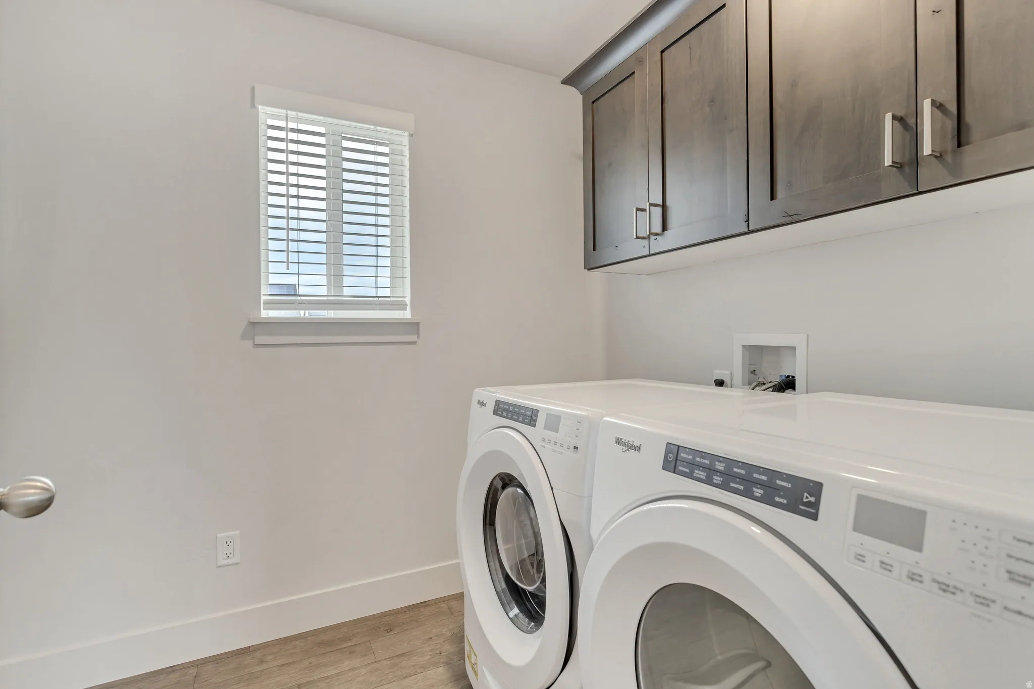 Upper cabinetry with contemporary hardware, wood-finish flooring, and a single window with blinds