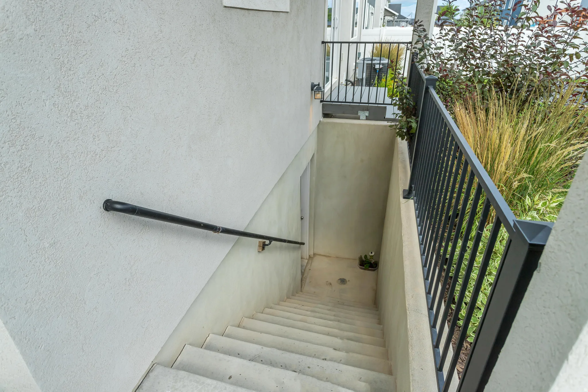 Concrete exterior staircase featuring a wrought iron handrail and a stucco finish wall