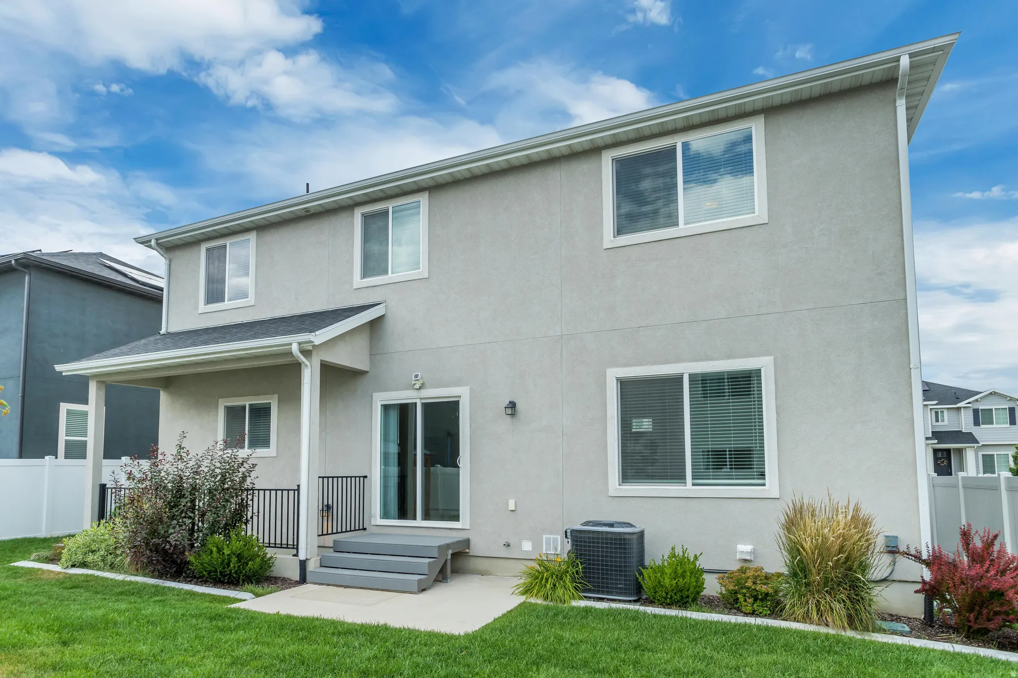 Stucco exterior with multiple windows, covered patio, sliding glass door, and a manicured lawn