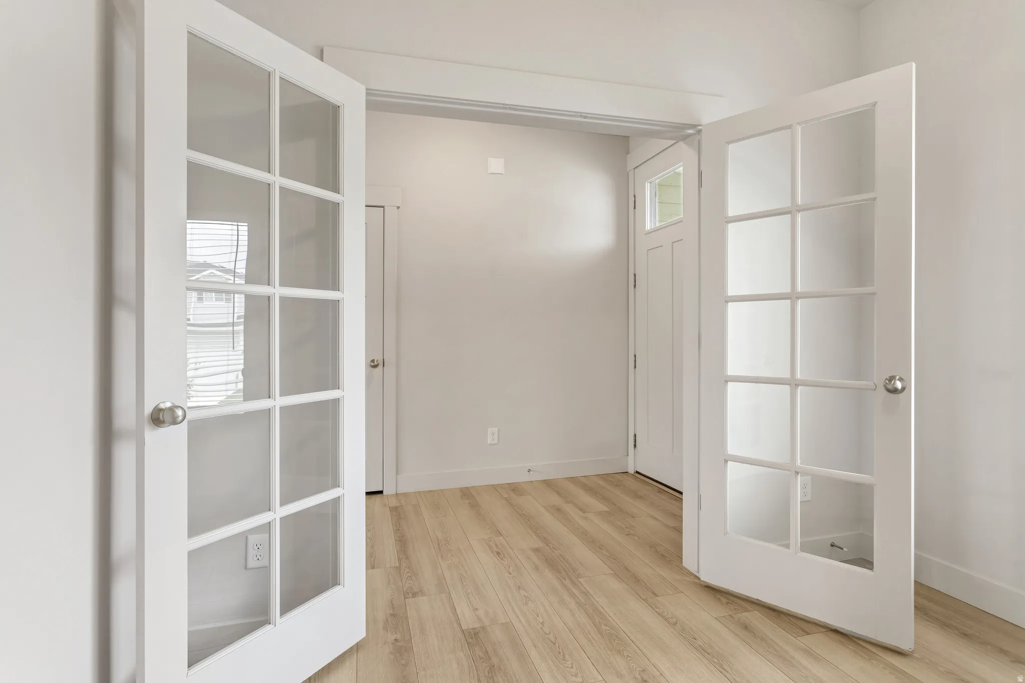 French doors with glass panels, light wood-finish flooring, white trim, and a white interior door with a transom window